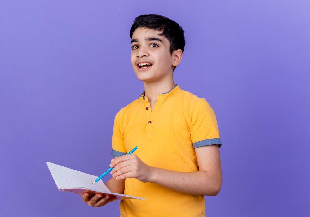 impressed-young-caucasian-boy-holding-note-pad-pencil-isolated-purple-wall-with-copy-space