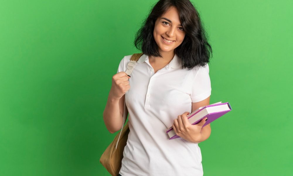 young-smiling-pretty-caucasian-schoolgirl-wearing-back-bag-holds-books-looking-camera-green-with-copy-space